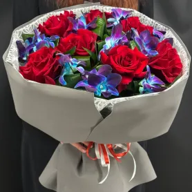 букет из красных французских роз и сине-фиолетовых орхидей с декоративной зеленью в упаковке
