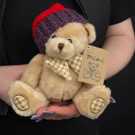 мягкая игрушка медвежонок бежевого, сиреневого и молочного цвета в вязаной шапке